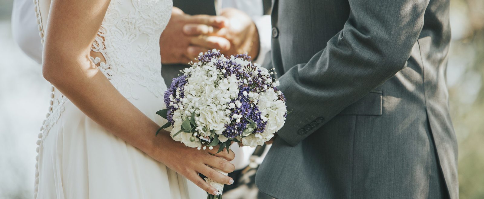 Mariée tenant un bouquet de fleurs blanches et violettes à côté du marié